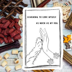 May include: A black and white sticker with the text "LEARNING TO LOVE MYSELF AS MUCH AS MY DOG" and an illustration of a hand high-fiving a dog's paw. The sticker is surrounded by dog treats of various shapes and colors.