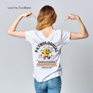 Könnte beinhalten: Weißes T-Shirt mit einer gelben Comicfigur und dem Text "Pathological People Pleaser" auf der Rückseite. Der Text "Est. 2022" und "Love You Too" befinden sich ebenfalls auf dem Shirt.
