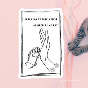 May include: A black and white sticker with the text "LEARNING TO LOVE MYSELF AS MUCH AS MY CAT." The sticker features a hand high-fiving a cat paw, with paw prints below. The background is pink.