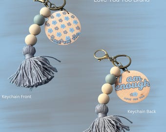 May include: Keychains with wooden round charms, tassels, and beads. One keychain has a floral pattern and the text "Love You Too". The other keychain has the text "I am enough". Both keychains have a gold-colored clasp.