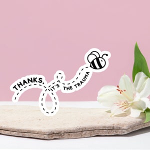Peut inclure: Un autocollant blanc avec du texte noir et un graphique d'abeille. Le texte dit "Merci, c'est le traumatisme". L'abeille vole vers la droite, laissant une ligne pointillée derrière elle.