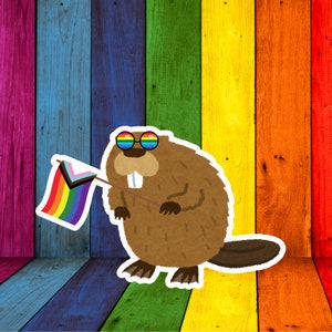 Può includere: Un castoro marrone dei cartoni animati con occhiali da sole arcobaleno e una bandiera arcobaleno con un simbolo del trans pride. Lo sfondo è composto da assi di legno verticali colorate, che rappresentano la bandiera LGBTQ+.