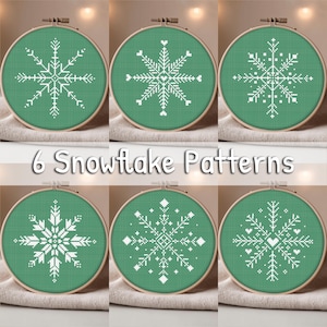 May include: Six embroidery hoops featuring white snowflake designs on green fabric. The hoops are displayed on a neutral fabric. The text "6 Snowflake Patterns" is below the hoops.