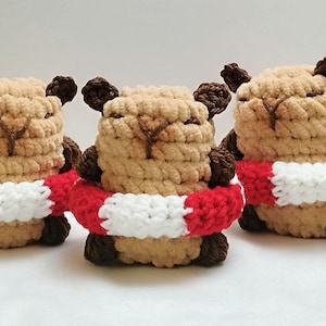 May include: Three handmade crochet bear figures. Each bear is beige with brown accents, including ears and paws. They wear a red and white striped scarf around their necks. The bears are arranged closely together.
