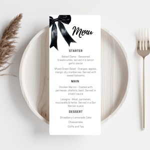 May include: A white menu card with a black bow illustration and the word "Menu" at the top. The menu lists starters, main courses, and desserts, including Baked Clams, Chicken Martini, and Strawberry-Lemonade Cake. The card is on a white plate with a gold fork.