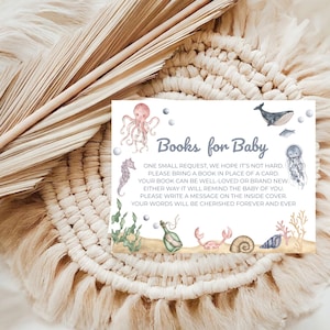 Puede incluir: Una tarjeta de invitación para baby shower con el texto "Books for Baby" e ilustraciones con temática marina. La tarjeta presenta un pulpo, un caballito de mar, una ballena, una medusa y otras criaturas marinas. La tarjeta está sobre un fondo beige tejido.