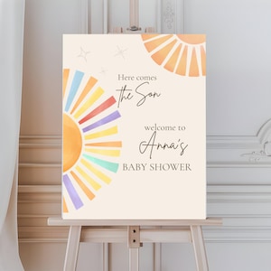 Puede incluir: Un letrero de bienvenida para baby shower sobre un caballete. El letrero tiene un fondo crema con diseños de sol en acuarela en naranja, amarillo, morado y azul. El texto dice "Here comes the Son" y "welcome to Anna's BABY SHOWER."