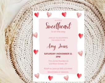 May include: A white invitation card with a pink border and red heart accents. The text reads "A Little Sweetheart is on the way" and includes details for a baby shower, including the name Amy Jones, date, time, and location.