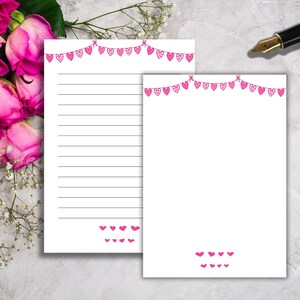 Puede incluir: Dos tarjetas blancas en blanco con guirnaldas de corazones rosas en la parte superior. Las tarjetas tienen espacio de escritura rayado y una fila de corazones rosas en la parte inferior.