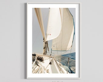 May include: A white sailboat with a large sail billowing in the wind. The boat is sailing on a blue ocean with a clear sky above.