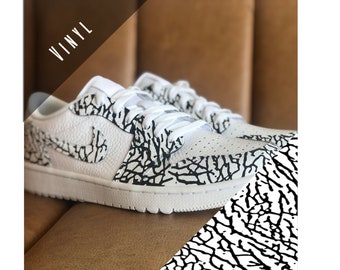 May include: White sneakers with black patterned accents. The shoes feature a textured design on the sides and toe, with white laces and soles. The word "VINYL" is in the upper left corner.