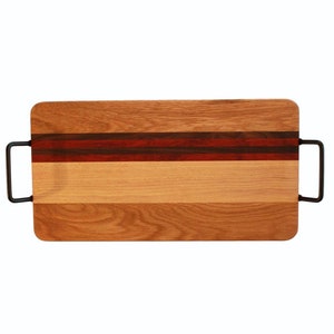 May include: A rectangular wooden cutting board with two black metal handles. The board is made of multiple wood types, including a red and brown stripe.