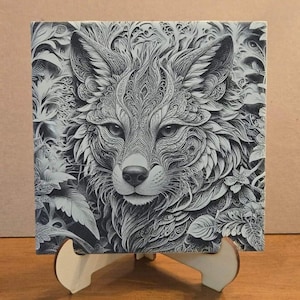May include: A black and white detailed illustration of a wolf's face with intricate patterns and designs. The wolf is surrounded by foliage and flowers. The image is printed on a square tile and displayed on a wooden stand.