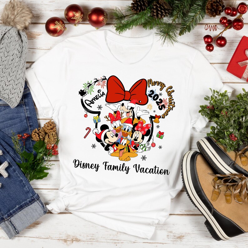 May include: White t-shirt featuring a Disney family graphic with Mickey, Minnie, Donald, Daisy, and Goofy. The design includes a red bow, the words "Merry Christmas 2025", and "Disney Family Vacation".