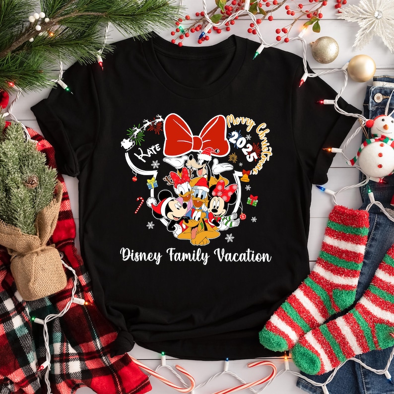 May include: Black t-shirt featuring a festive Disney design. The design includes Mickey and Minnie Mouse, Donald and Daisy Duck, and Goofy, with a large red bow and the text "Merry Christmas 2025" and "Disney Family Vacation".