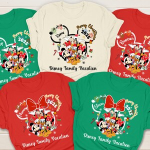 May include: A collection of Christmas-themed t-shirts in various colors, featuring Disney characters. Each shirt has a Mickey Mouse head design with the text "Merry Christmas 2025" and "Disney Family Vacation". Some shirts have additional text like "Mommy", "Brother", or "Sister".