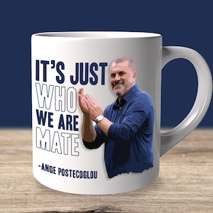 Könnte beinhalten: Weiße Keramiktasse mit einer blauen und weißen Grafik eines Mannes, der klatscht, und dem Text "It's just who we are mate - Ange Postecoglou"