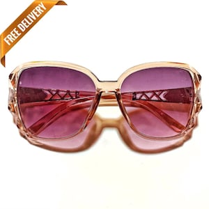 May include: A pair of brown plastic sunglasses with purple lenses. The lenses have a decorative pattern of lines.