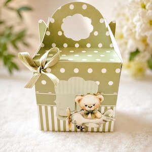 May include: A sage green paper gift box featuring a white polka dot pattern on the top half and vertical white stripes on the bottom half. The box has a die-cut handle, a light green ribbon bow, and a decorative cutout of a teddy bear in a plane.