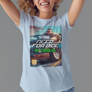 Peut inclure: T-shirt bleu clair avec un motif d'un homme dans une voiture, avec le texte "NEED FOR BIDE" et "HOT CHOCOLATE". Le graphisme est de style jeu vidéo avec une classification "12+".