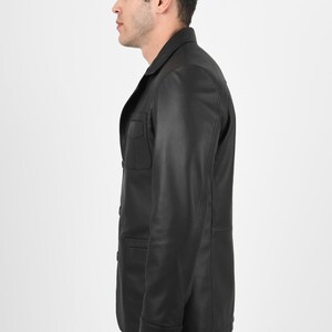 May include: A black leather jacket with a classic design. The jacket features a collared neckline, buttoned front, and two chest pockets. The model is wearing the jacket with dark jeans.