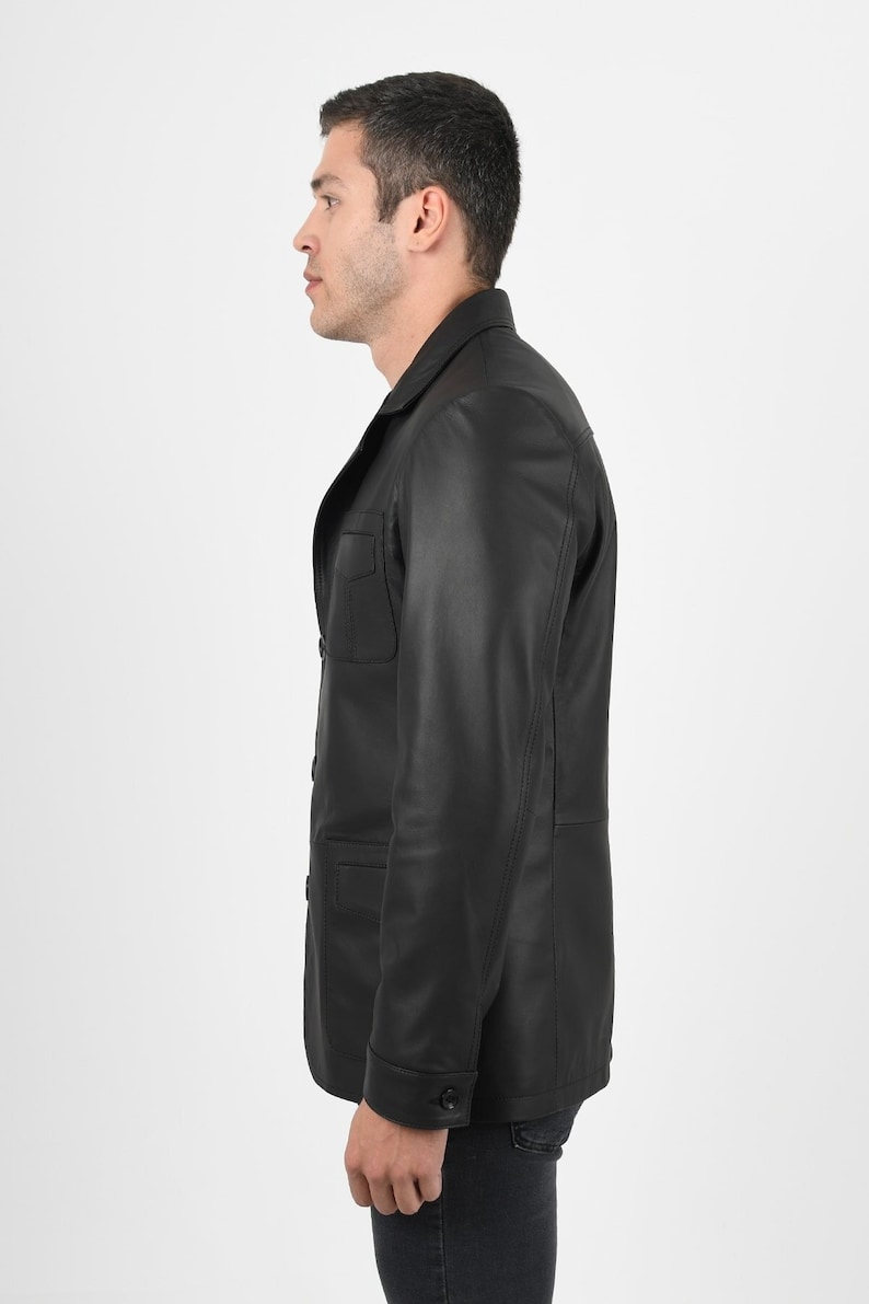 May include: A black leather jacket with a classic design. The jacket features a collared neckline, buttoned front, and two chest pockets. The model is wearing the jacket with dark jeans.