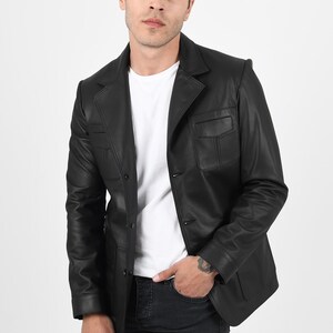 May include: A black leather blazer with a notched lapel, two front pockets, and a two-button closure. The blazer is worn over a white t-shirt and paired with black jeans. The model is standing in front of a white background.