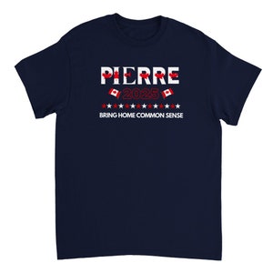 Könnte beinhalten: Ein marineblaues T-Shirt mit weißem Text, der "PIERRE 2025" und "BRING HOME COMMON SENSE" lautet. Über und unter dem Text befinden sich kleine kanadische Flaggen.