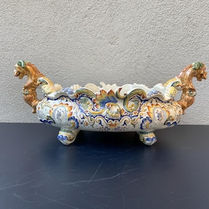 Peut inclure: Un pot en céramique blanche avec un motif floral bleu, jaune et vert. Le pot a deux poignées en forme de dragon et trois pieds.
