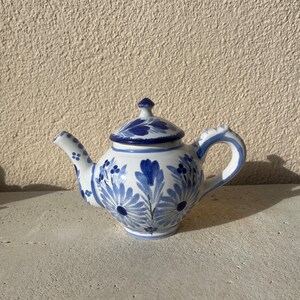 Op de afbeelding: Een klein blauw en wit aardewerken theepot met een bloemenmotief. De theepot heeft een deksel en een tuit.