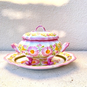 Könnte beinhalten: Eine weiße Keramik-Servierplatte mit einem rosa und gelben Blumendesign. Die Platte hat drei Füße und einen Deckel. Die Platte steht auf einer weißen Oberfläche.