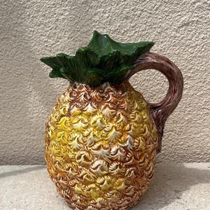 Peut inclure: Pichet en céramique en forme d'ananas, avec un dessus feuillu vert et une anse marron. Le pichet est jaune, marron et crème, avec une surface texturée. Ce pichet décoratif est idéal pour servir des boissons.