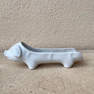 Könnte beinhalten: Weiße Keramik-Schale in Form eines Schweins mit einem langen, schmalen Körper und vier Beinen. Die Schale ist für kleine Gegenstände wie Besteck oder Schmuck gedacht.