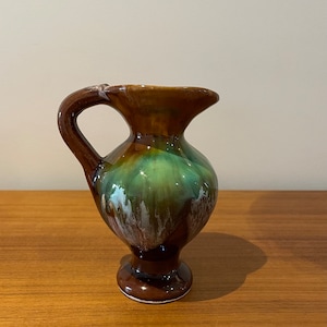 May include: A small brown and green ceramic pitcher with a white glaze. The pitcher has a rounded body and a small spout.