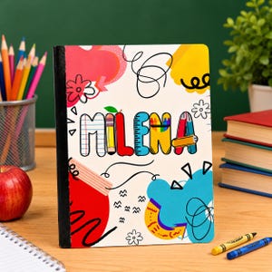 May include: A rectangular notebook with a white cover featuring the name MILENA in colorful, patterned block letters. The design includes vibrant red, yellow, and blue abstract shapes, black scribbles, and small flower illustrations.