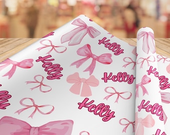 May include: White wrapping paper with a repeating pattern of pink bows and the name "Kelly" in a cursive font. The bows vary in style and size, creating a festive design.