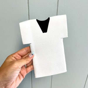 May include: White foam can cooler shaped like a doctor's scrubs with a black V-neck.