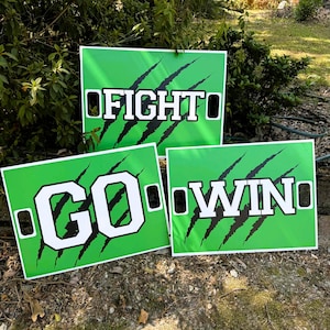 May include: Three rectangular green signs featuring black claw marks and white block lettering. The top sign reads FIGHT, the bottom left sign reads GO, and the bottom right sign reads WIN. Each sign has black rectangular cutouts on the sides.