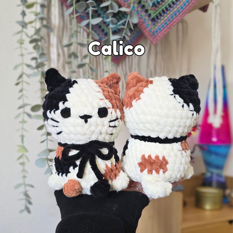 May include: Two handmade crochet cat plushies featuring a calico pattern with white, black, and orange yarn. The front cat has a black yarn bow around its neck. The word Calico is printed in white text above the plushies. The yarn texture is soft.