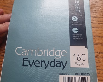 May include: A blue notebook with a white label that says "Cambridge Everyday" and "160 Pages". The label also includes a barcode and the text "Made in the EU" and "100080235".