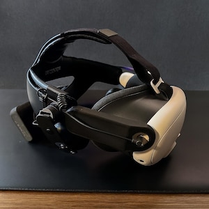 Könnte beinhalten: Ein Virtual-Reality-Headset in Schwarz und Weiß. Es verfügt über verstellbare Riemen, einen oberen Kopfgurt und einen seitlichen Verstellmechanismus. Das Headset ist für immersives Gaming und virtuelle Erlebnisse konzipiert.
