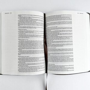 May include: An open book with white pages and black text, featuring a dark brown cover. The book is lying flat on a white surface. The text is small and densely packed, suggesting a religious or scholarly work.