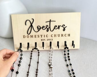 Può includere: Un organizzatore per gioielli da parete in legno con il testo "Roesters Domestic Church Est. 2013" e otto ganci per appendere collane.