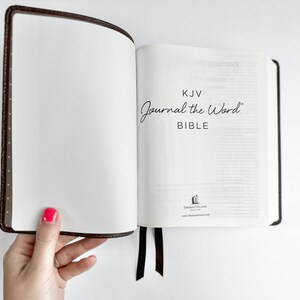 May include: Open KJV Journal the Word Bible with a brown leather cover and a black ribbon bookmark. The text "Journal the Word BIBLE" is visible on the right page. The left page is blank.