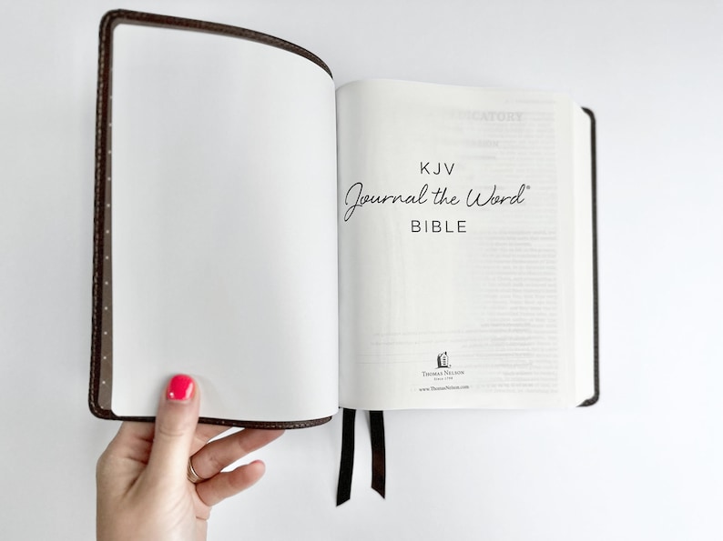 May include: Open KJV Journal the Word Bible with a brown leather cover and a black ribbon bookmark. The text "Journal the Word BIBLE" is visible on the right page. The left page is blank.