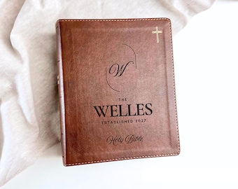 May include: A brown leather-bound Holy Bible featuring a gold cross icon at the top, a large letter W inside an oval, and the text THE WELLES ESTABLISHED 2027 engraved on the front cover. The book has visible stitching along the edges.