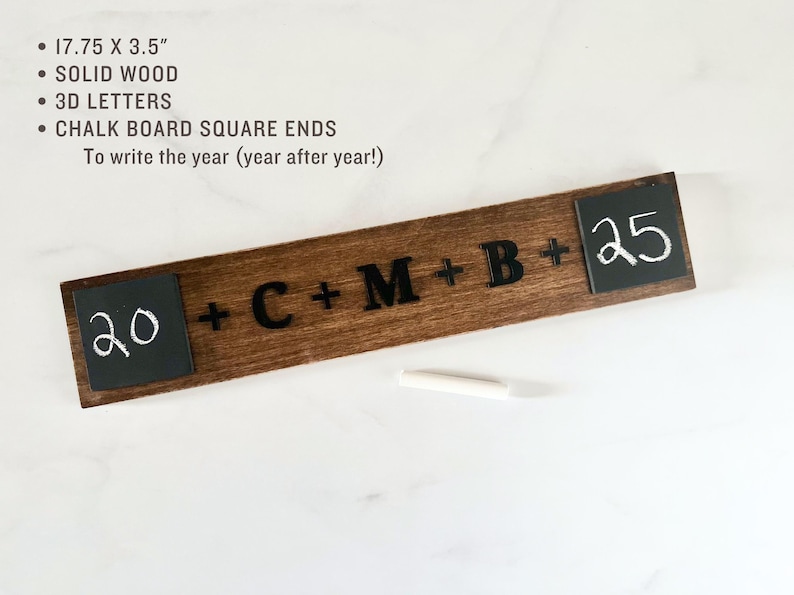 May include: A wooden sign with black lettering that reads "20 + C + M + B + 25". The sign has two small chalkboard squares on either end, one with the number "20" written in white chalk and the other with the number "25" written in white chalk. The sign is 45.1 cm by 8.9 cm.