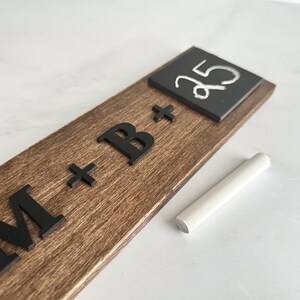 May include: A wooden sign with the text "M + B +" and a small chalkboard with the number "35" written on it. A piece of chalk is lying next to the sign.