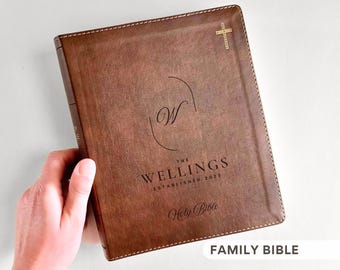 May include: A brown leather-bound Holy Bible with gold cross and text. The cover features the family name "The Wellings" and "Established 2023" with a stylized "W" monogram. The words "Holy Bible" are also visible.