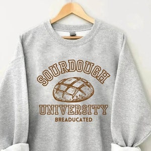 May include: A gray sweatshirt with the text "SOURDOUGH UNIVERSITY BREADUCATED" in brown lettering. A drawing of a sourdough loaf is above the text.